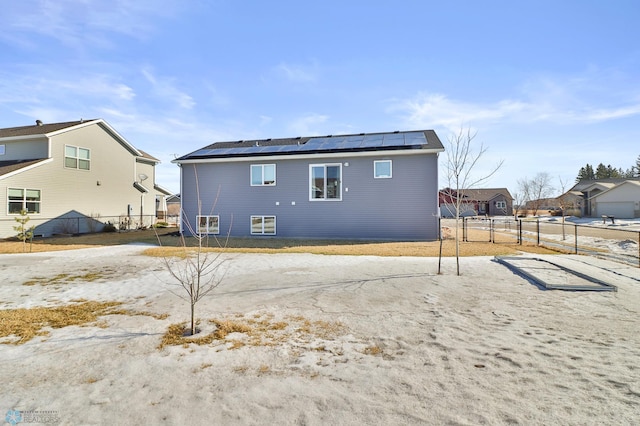 rear view of house featuring roof mounted solar panels and fence