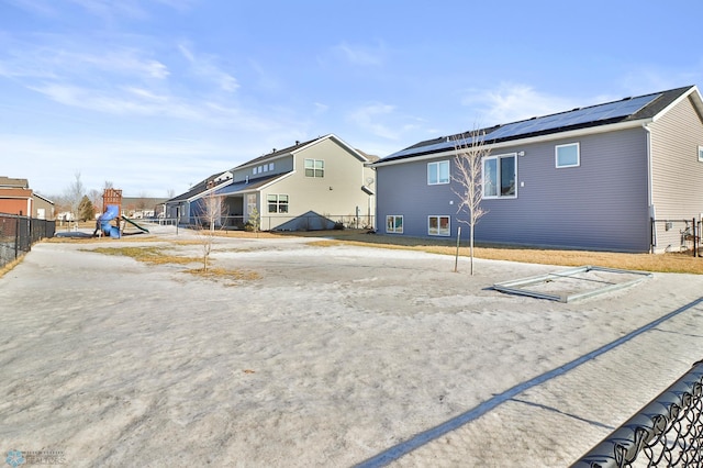 rear view of house with a residential view, a playground, fence, and solar panels