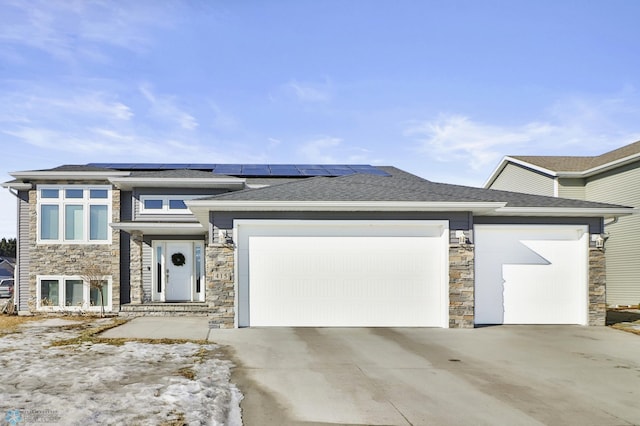 prairie-style house featuring an attached garage, stone siding, roof mounted solar panels, and concrete driveway