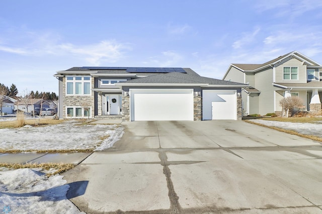 view of front of home with solar panels, stone siding, an attached garage, and driveway