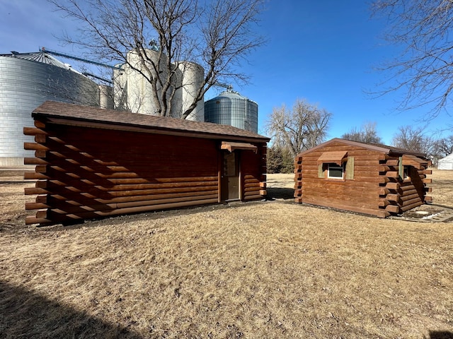 view of property exterior with a storage shed, log exterior, a chimney, and an outdoor structure