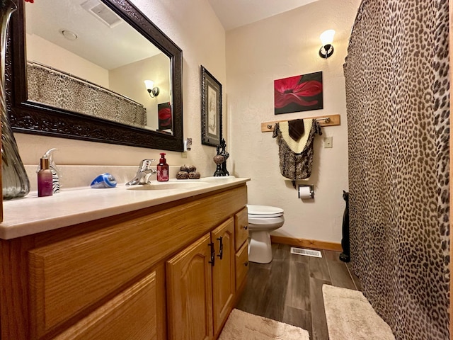 bathroom with baseboards, visible vents, toilet, wood finished floors, and vanity