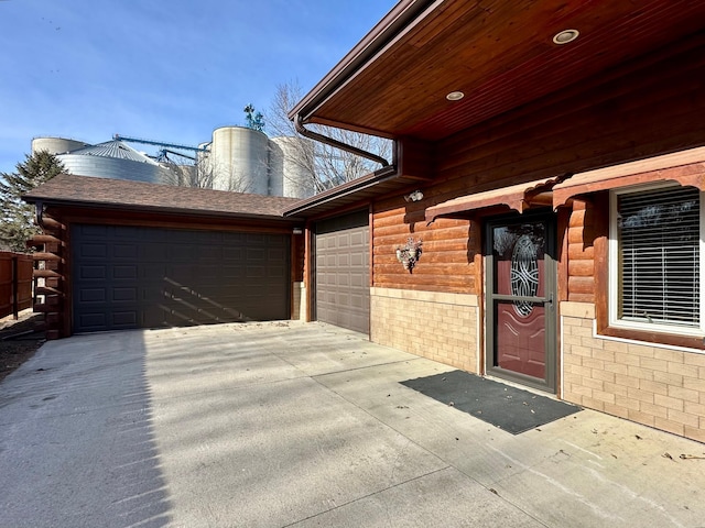 view of exterior entry with a garage, driveway, a shingled roof, and log exterior