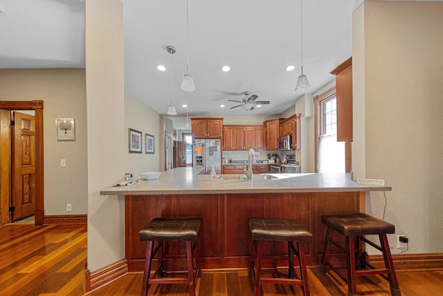 kitchen featuring stainless steel appliances, dark wood-style flooring, a sink, and a peninsula