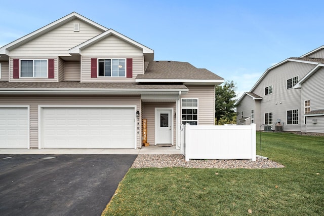 view of front of home with driveway, a garage, a shingled roof, fence, and a front lawn