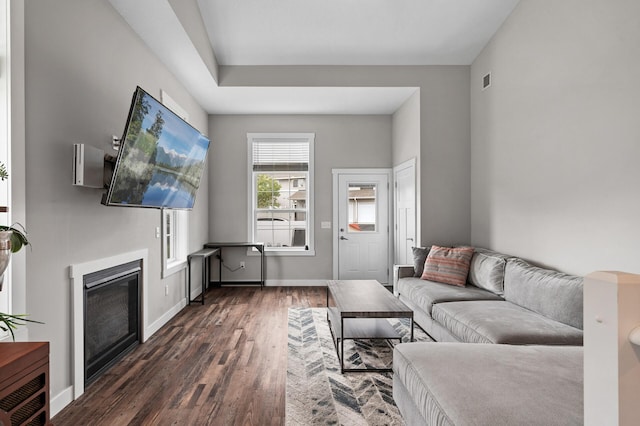 living room featuring visible vents, baseboards, dark wood-style flooring, and a glass covered fireplace