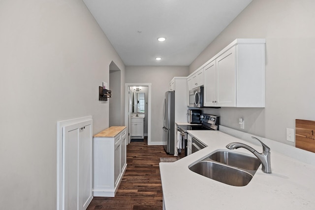 kitchen featuring baseboards, white cabinets, dark wood finished floors, stainless steel appliances, and a sink