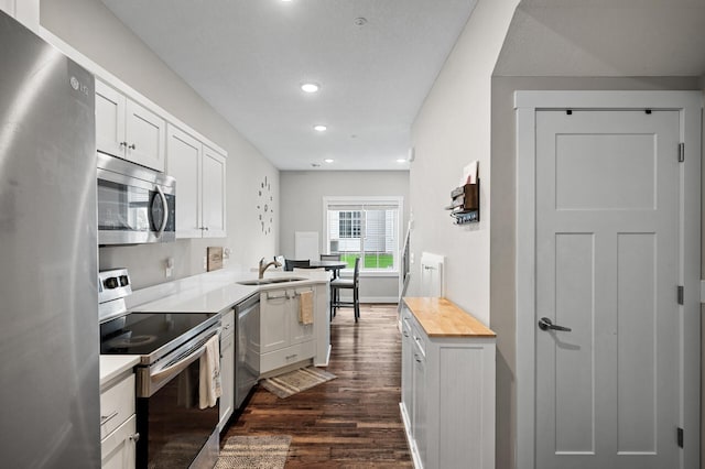 kitchen with dark wood-style flooring, appliances with stainless steel finishes, white cabinetry, a sink, and butcher block countertops