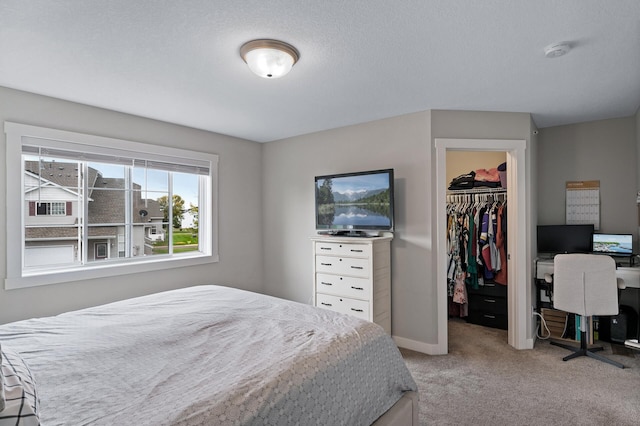 bedroom featuring a walk in closet, a closet, light carpet, and baseboards