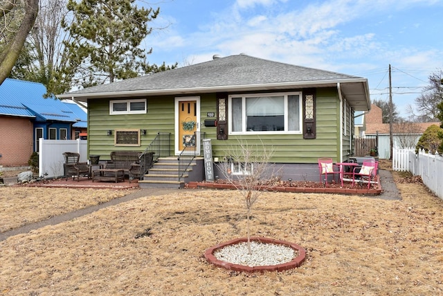 view of front facade with a shingled roof, fence, and a patio