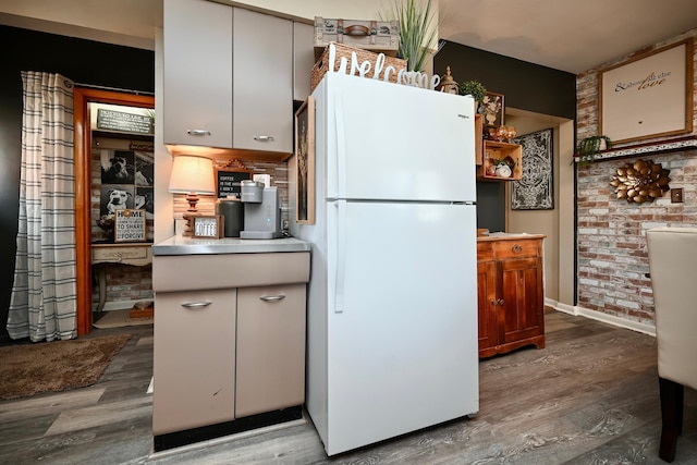 kitchen with brick wall, baseboards, wood finished floors, and freestanding refrigerator