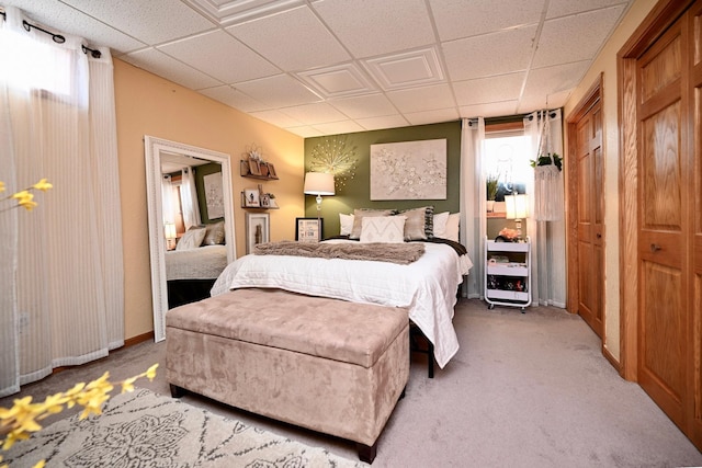 bedroom featuring light colored carpet, a drop ceiling, and baseboards