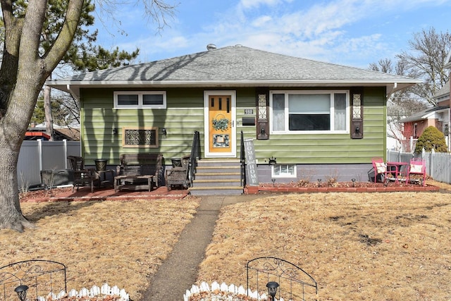 bungalow-style home with a shingled roof, entry steps, and fence