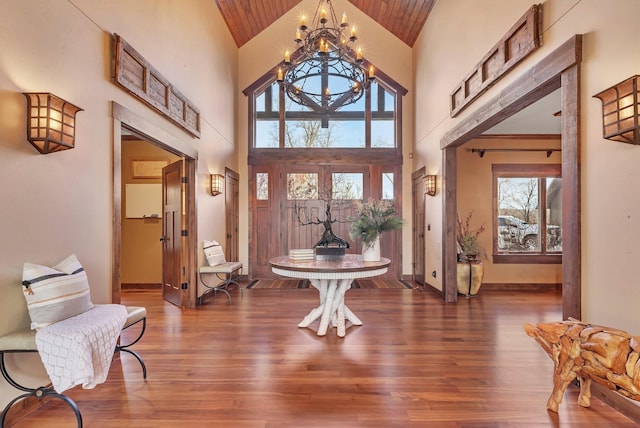 entrance foyer featuring a chandelier, high vaulted ceiling, wooden ceiling, wood finished floors, and baseboards