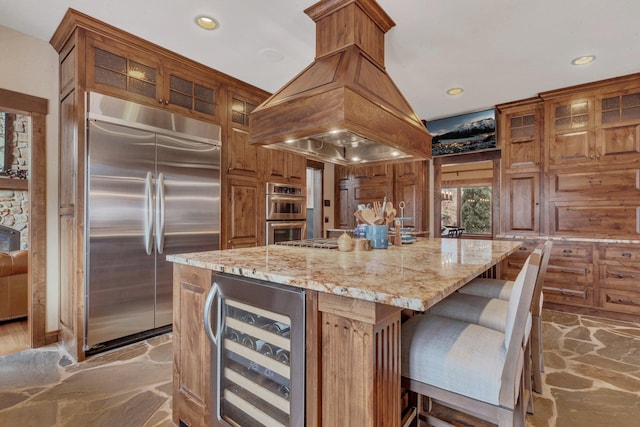 kitchen with wine cooler, stone flooring, light stone countertops, island exhaust hood, and stainless steel appliances