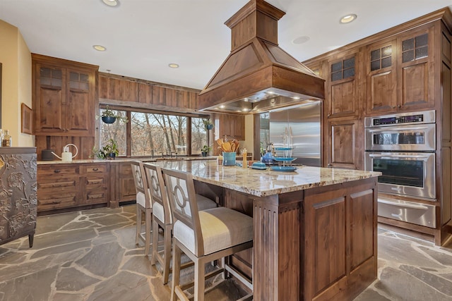 kitchen featuring a center island, a warming drawer, island exhaust hood, appliances with stainless steel finishes, and stone floors