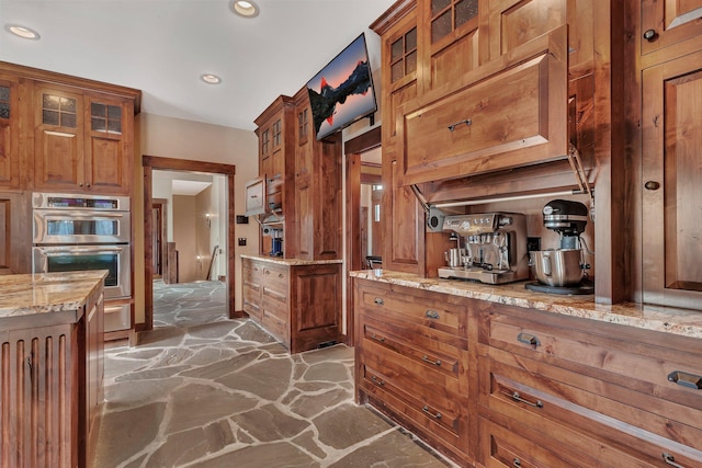 kitchen featuring brown cabinetry, stone flooring, double oven, and light stone countertops