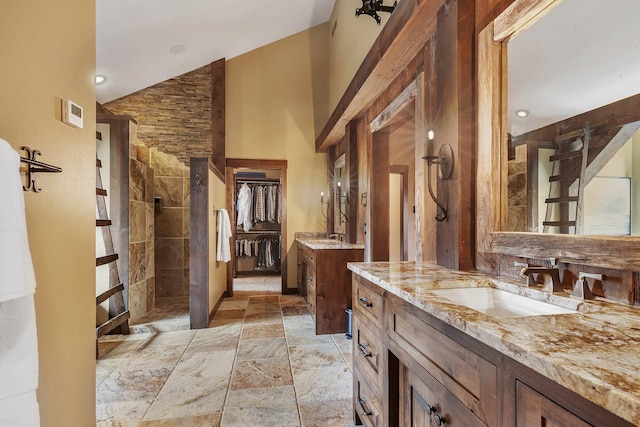 full bathroom featuring high vaulted ceiling, two vanities, a sink, a tile shower, and stone tile flooring