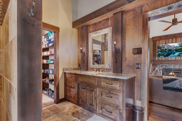 bathroom featuring visible vents, a ceiling fan, stone finish floor, a stone fireplace, and vanity