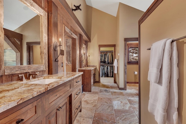 full bath with high vaulted ceiling, a walk in closet, vanity, and stone tile floors