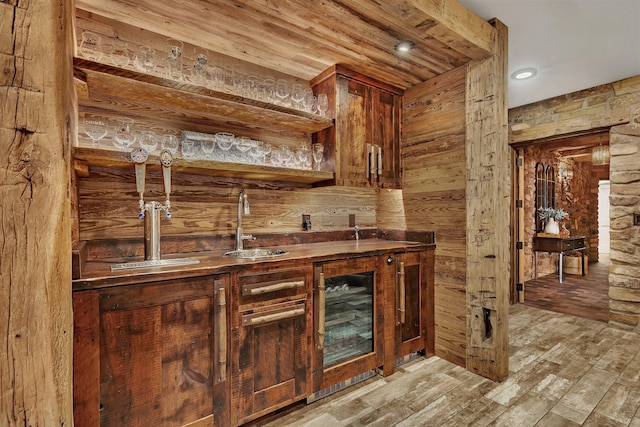 bar featuring light wood-style floors, indoor wet bar, a sink, and wood walls