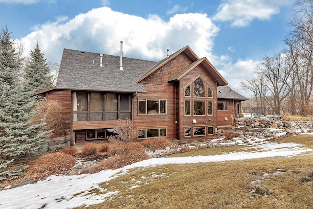 snow covered back of property with a sunroom and roof with shingles