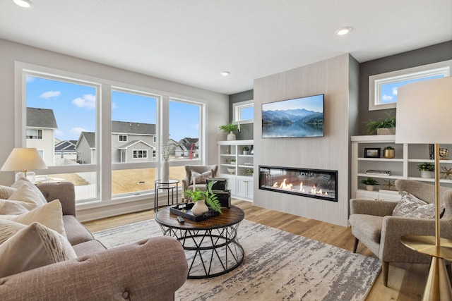 living room featuring a healthy amount of sunlight, light wood-style floors, recessed lighting, and a glass covered fireplace