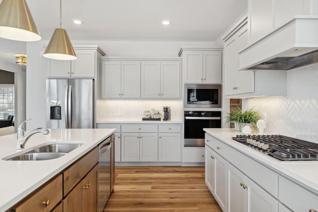 kitchen featuring stainless steel appliances, premium range hood, a sink, light countertops, and light wood-type flooring