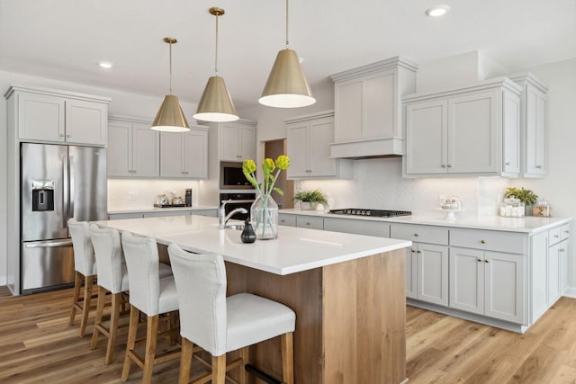 kitchen with a kitchen island with sink, appliances with stainless steel finishes, light wood-type flooring, and a breakfast bar