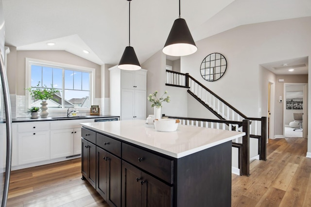 kitchen with light wood-style flooring, white cabinetry, vaulted ceiling, and a sink