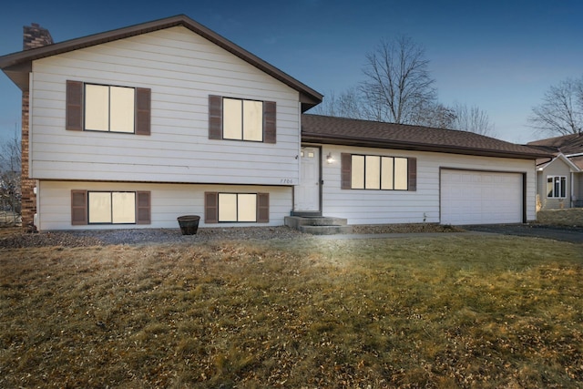 split level home with a garage, a chimney, aphalt driveway, and a front yard