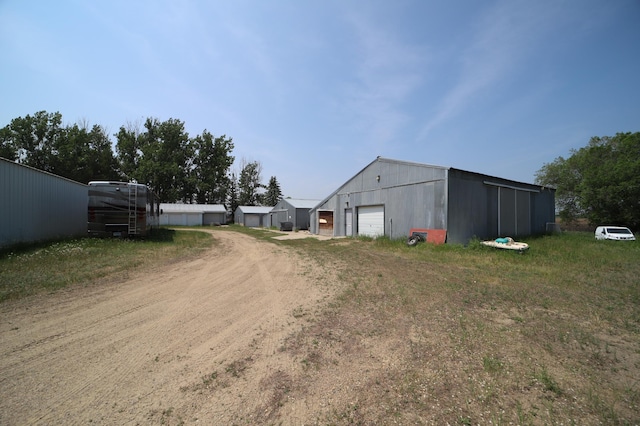 exterior space featuring dirt driveway, a detached garage, an outdoor structure, and an outbuilding