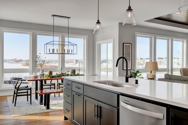 kitchen featuring light wood-style flooring, hanging light fixtures, light countertops, stainless steel dishwasher, and a sink