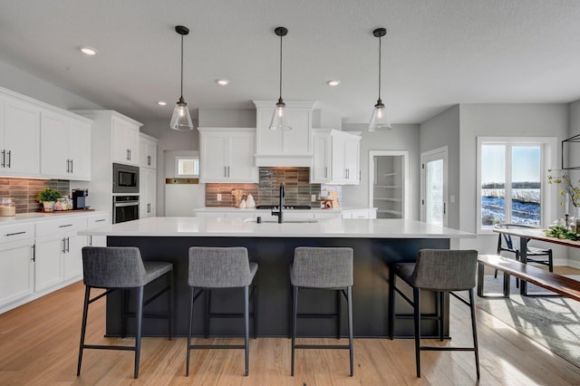 kitchen with stainless steel appliances, a sink, white cabinetry, light countertops, and an island with sink