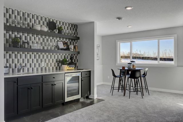 bar featuring indoor wet bar, dark colored carpet, a sink, a textured ceiling, and beverage cooler