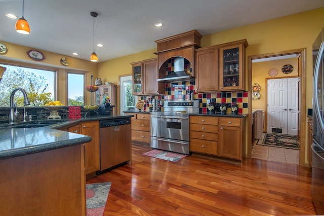 kitchen with appliances with stainless steel finishes, brown cabinetry, a sink, and wall chimney exhaust hood