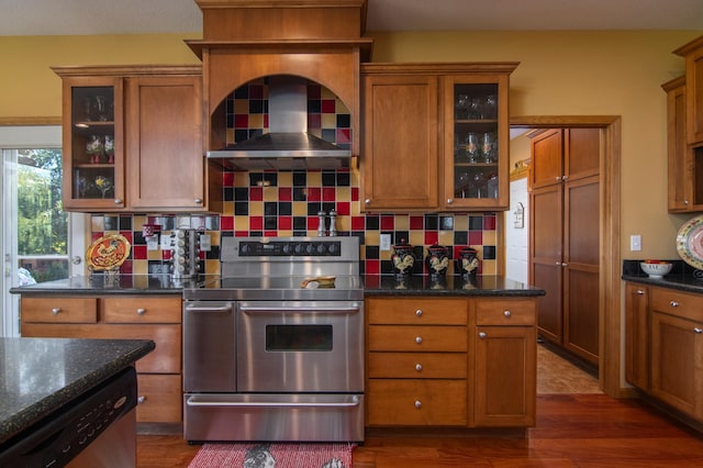 kitchen with dark wood-style floors, wall chimney exhaust hood, brown cabinets, stainless steel appliances, and backsplash