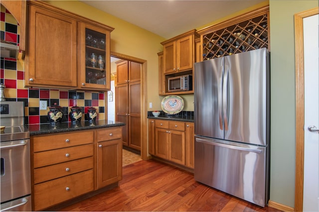 kitchen featuring stainless steel appliances, backsplash, brown cabinetry, glass insert cabinets, and wood finished floors