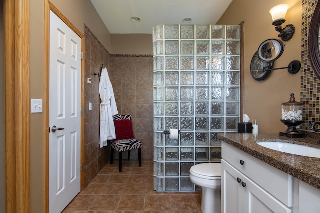 bathroom with tile walls, toilet, vanity, tile patterned flooring, and walk in shower