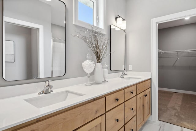 full bath featuring marble finish floor, double vanity, a sink, and a walk in closet