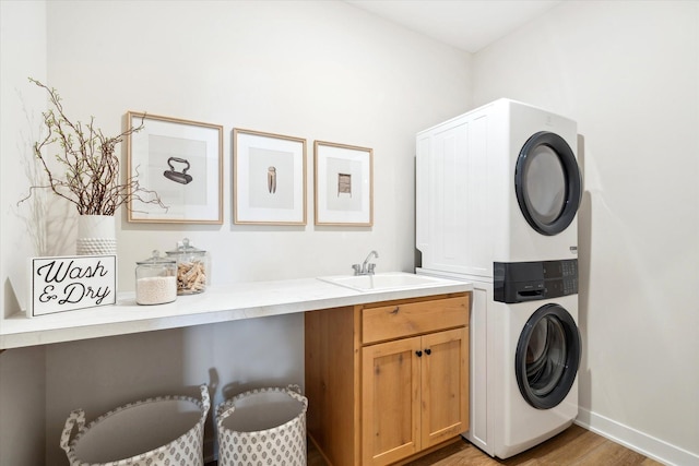 clothes washing area featuring cabinet space, light wood-style floors, stacked washer / dryer, a sink, and baseboards