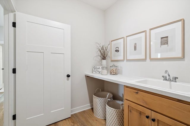 laundry room featuring light wood finished floors, baseboards, and a sink