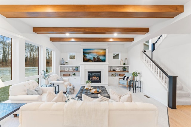 living room featuring visible vents, a glass covered fireplace, light wood-style flooring, beamed ceiling, and stairs