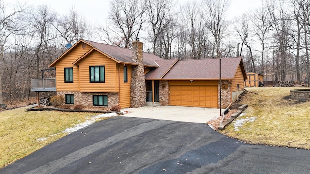 split level home featuring driveway, a shingled roof, a chimney, an attached garage, and a front lawn