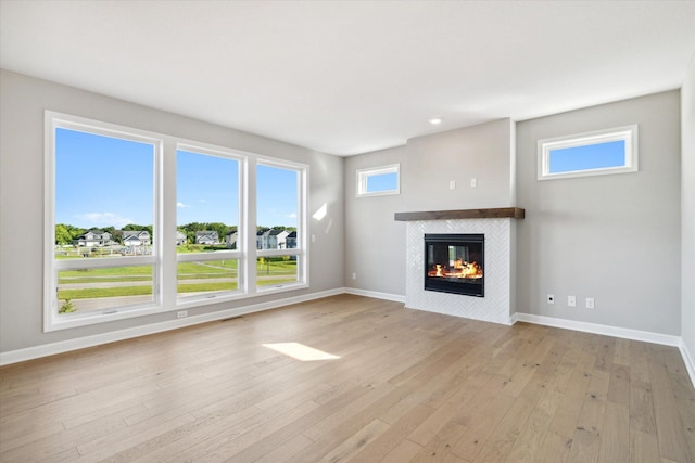 unfurnished living room with light wood-type flooring, a tile fireplace, and baseboards