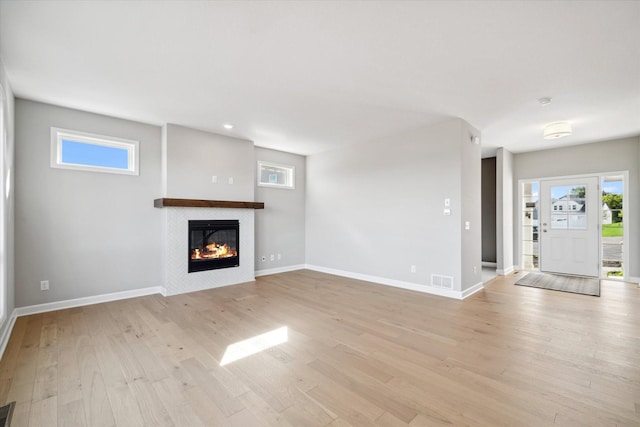 unfurnished living room featuring light wood-type flooring, visible vents, baseboards, and a tile fireplace