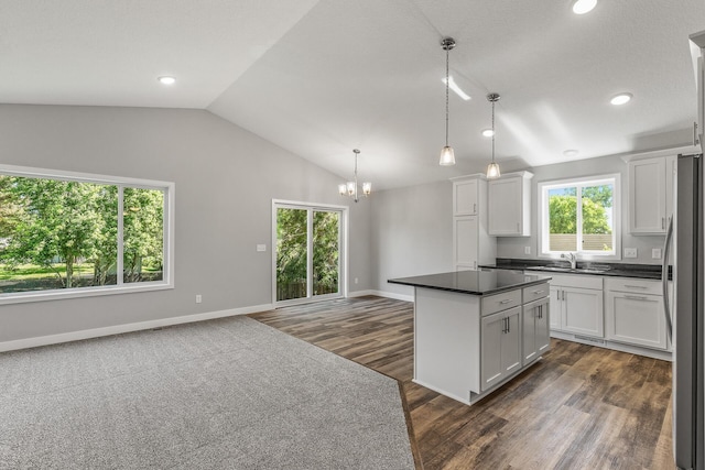 kitchen featuring white cabinets, dark countertops, a center island, freestanding refrigerator, and vaulted ceiling