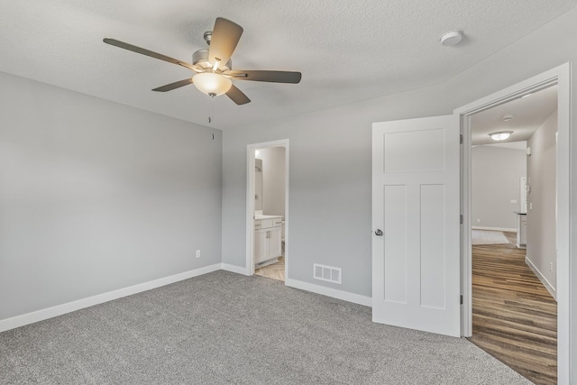 unfurnished bedroom featuring a textured ceiling, ensuite bathroom, light carpet, visible vents, and baseboards