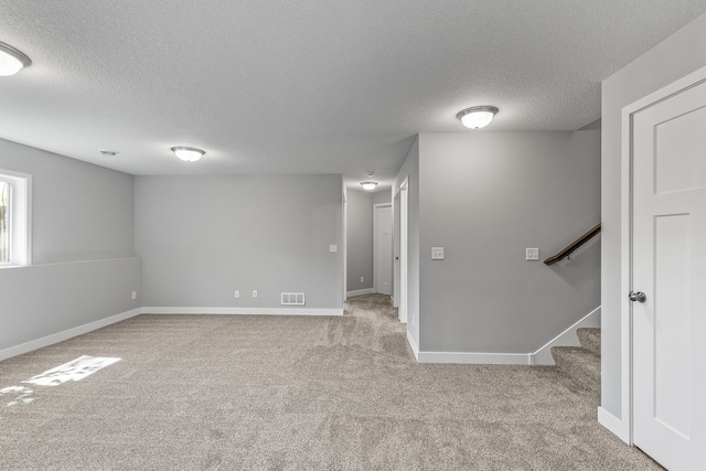 basement featuring baseboards, visible vents, stairway, a textured ceiling, and carpet flooring