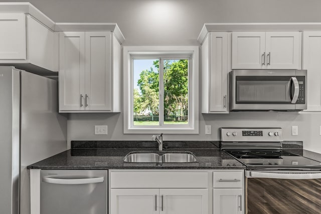 kitchen featuring appliances with stainless steel finishes, white cabinetry, a sink, wood finished floors, and dark stone counters